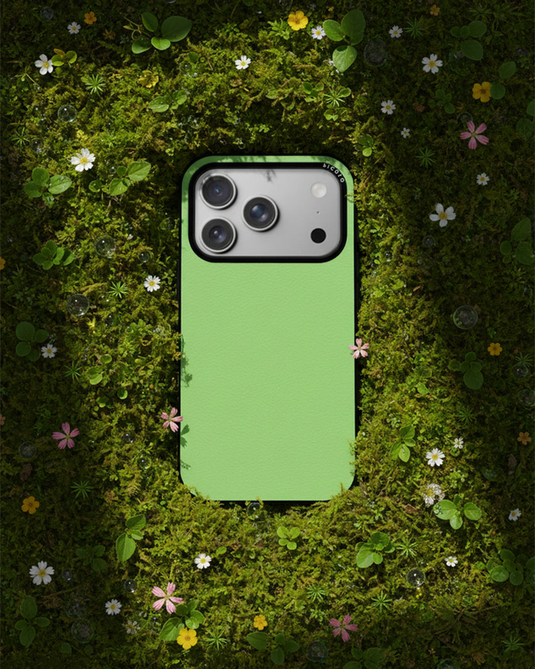Sicora Sage Green iPhone 17 Pro case made of SILIO pure silicone placed on a natural moss background with flowers.