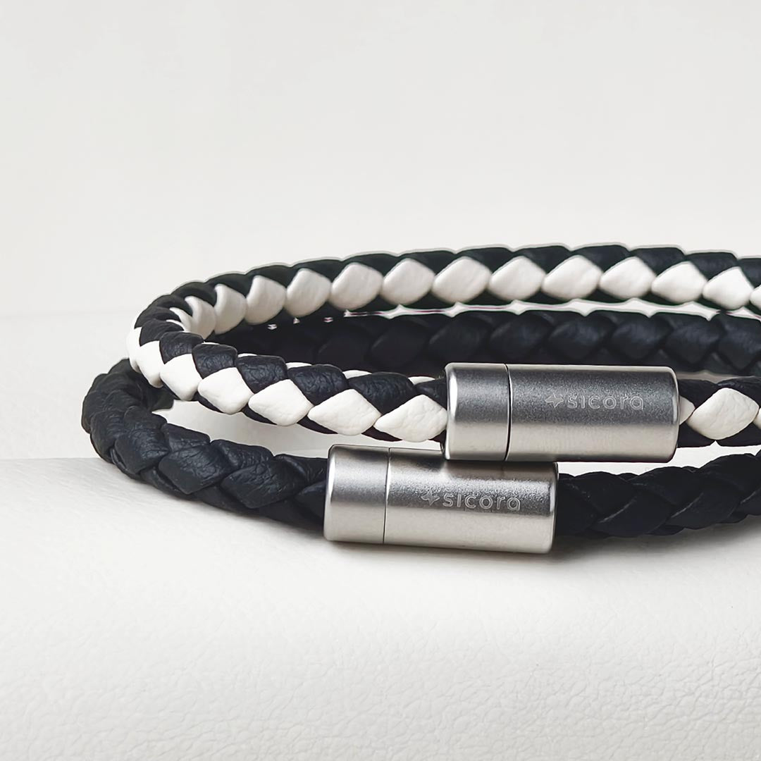 Sicora Black and white braided leather bracelets with stainless steel magnetic clasps engraved with the brand name 'sicora', displayed on a light gray textured surface.
