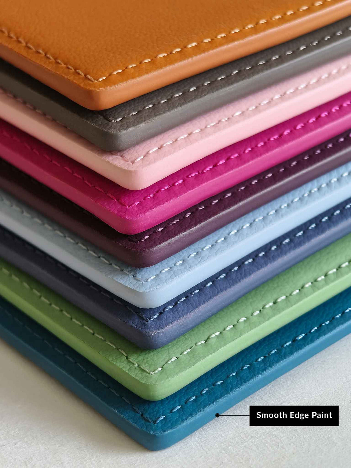 A stack of colorful sicora vegan leather badge holders with visible stitching, shown in shades of tan, gray, pink, magenta, purple, light blue, green, navy, and teal. 