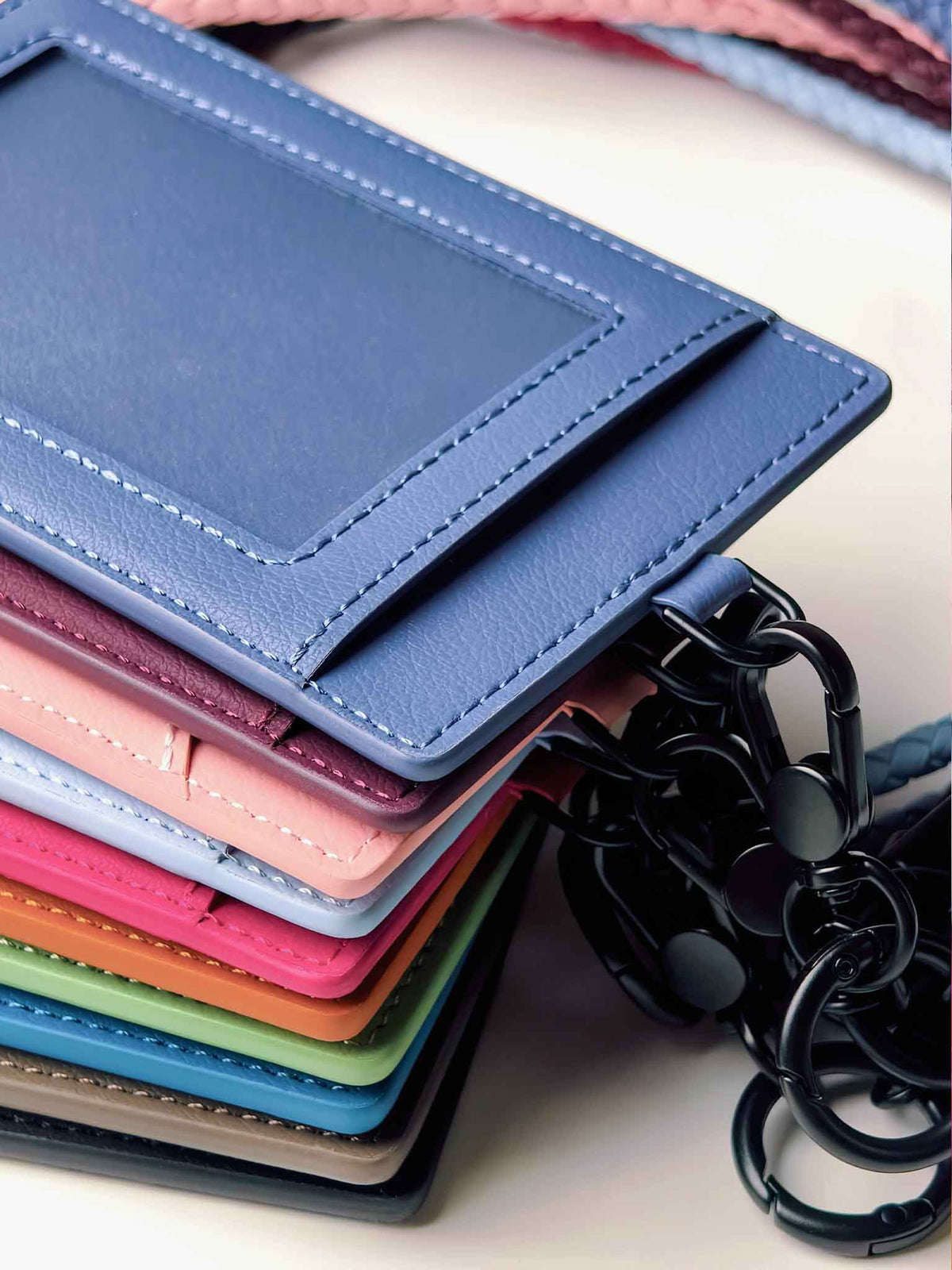 A stack of sicora vegan  leather ID badge holders in multiple colors, including blue, pink, purple, orange, green, and gray, each with a black keychain ring attachment.