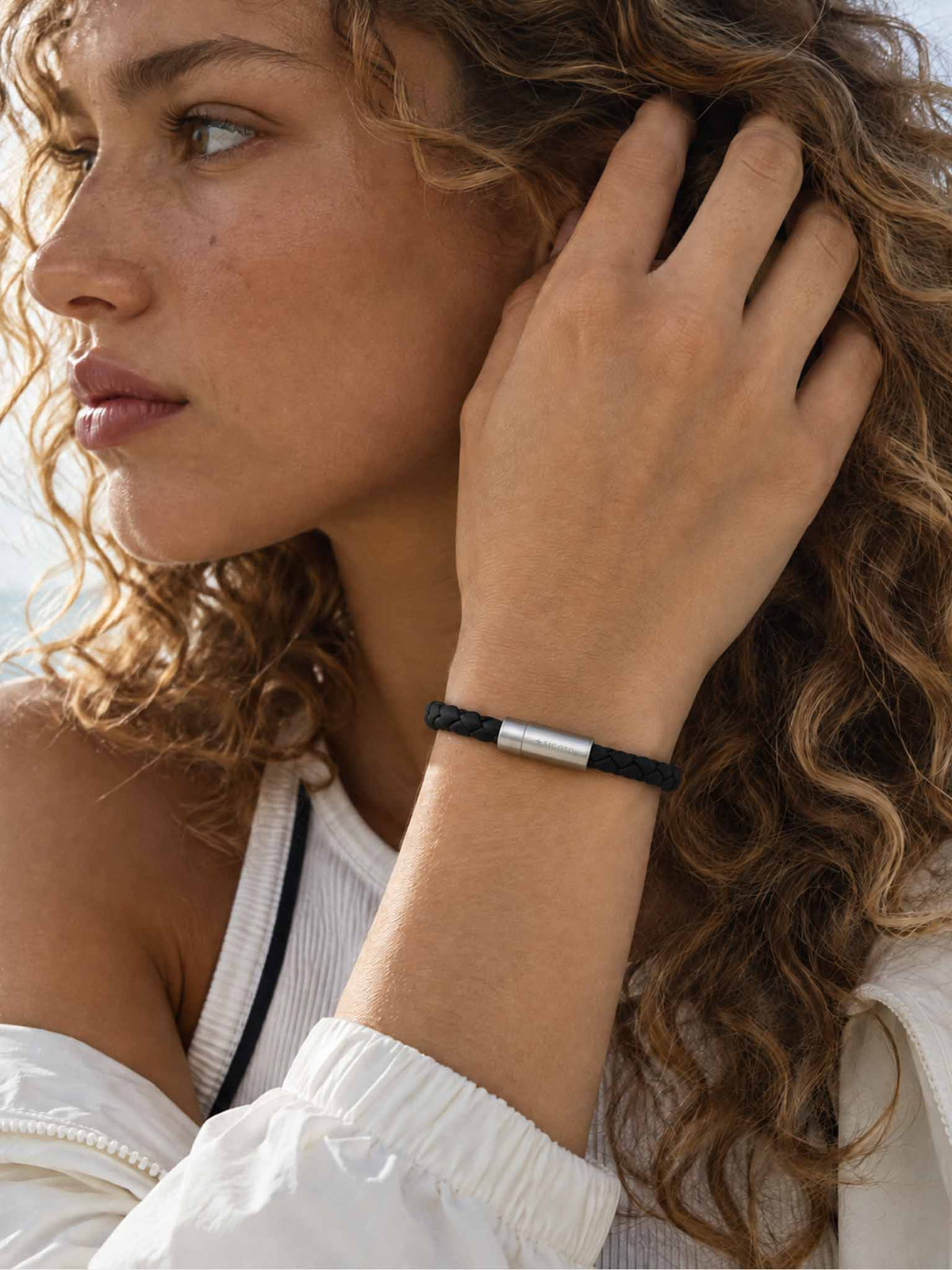 A close-up lifestyle shot of a woman wearing a sicora black braided silio silicone vegan leather bracelet with a stainless steel metal magnetic clasp on her wrist.