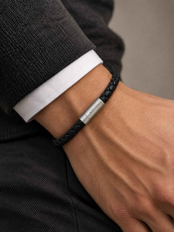 A close-up of a man's wrist wearing a sicora black braided leather bracelet with a stainless steel metal cylinder clasp.