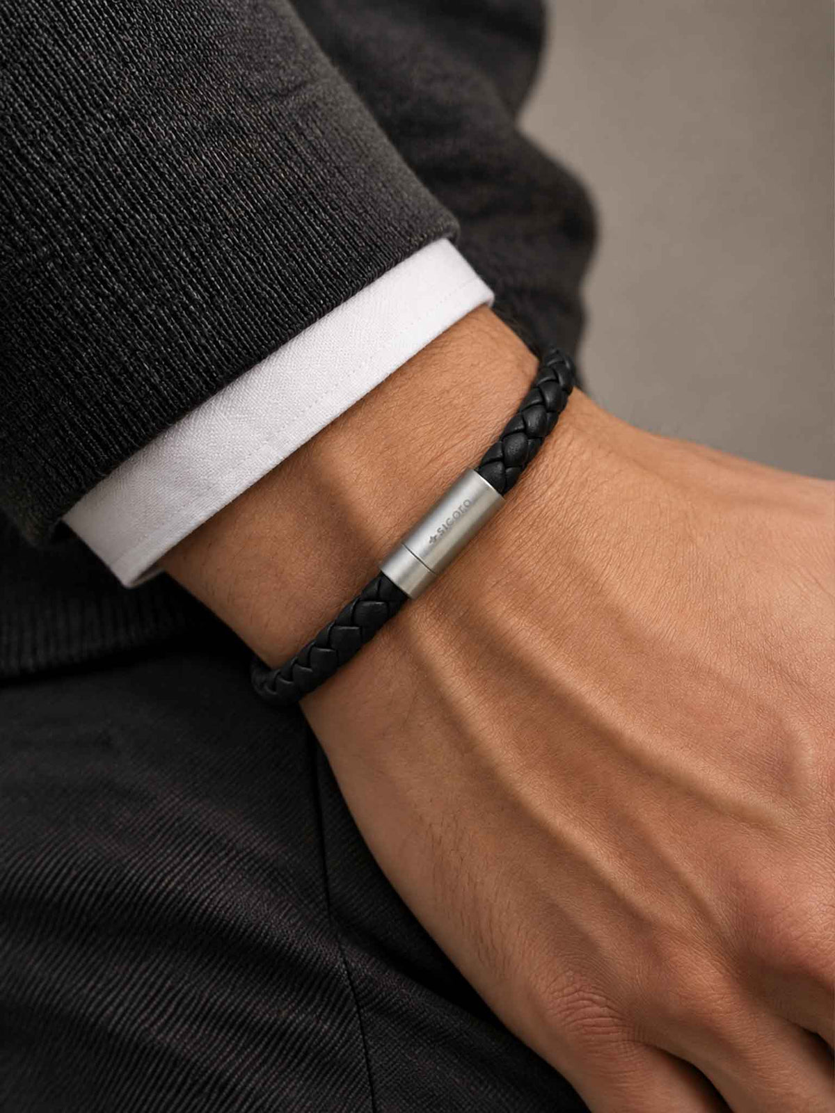 A close-up of a man's wrist wearing a sicora black braided leather bracelet with a stainless steel metal cylinder clasp.