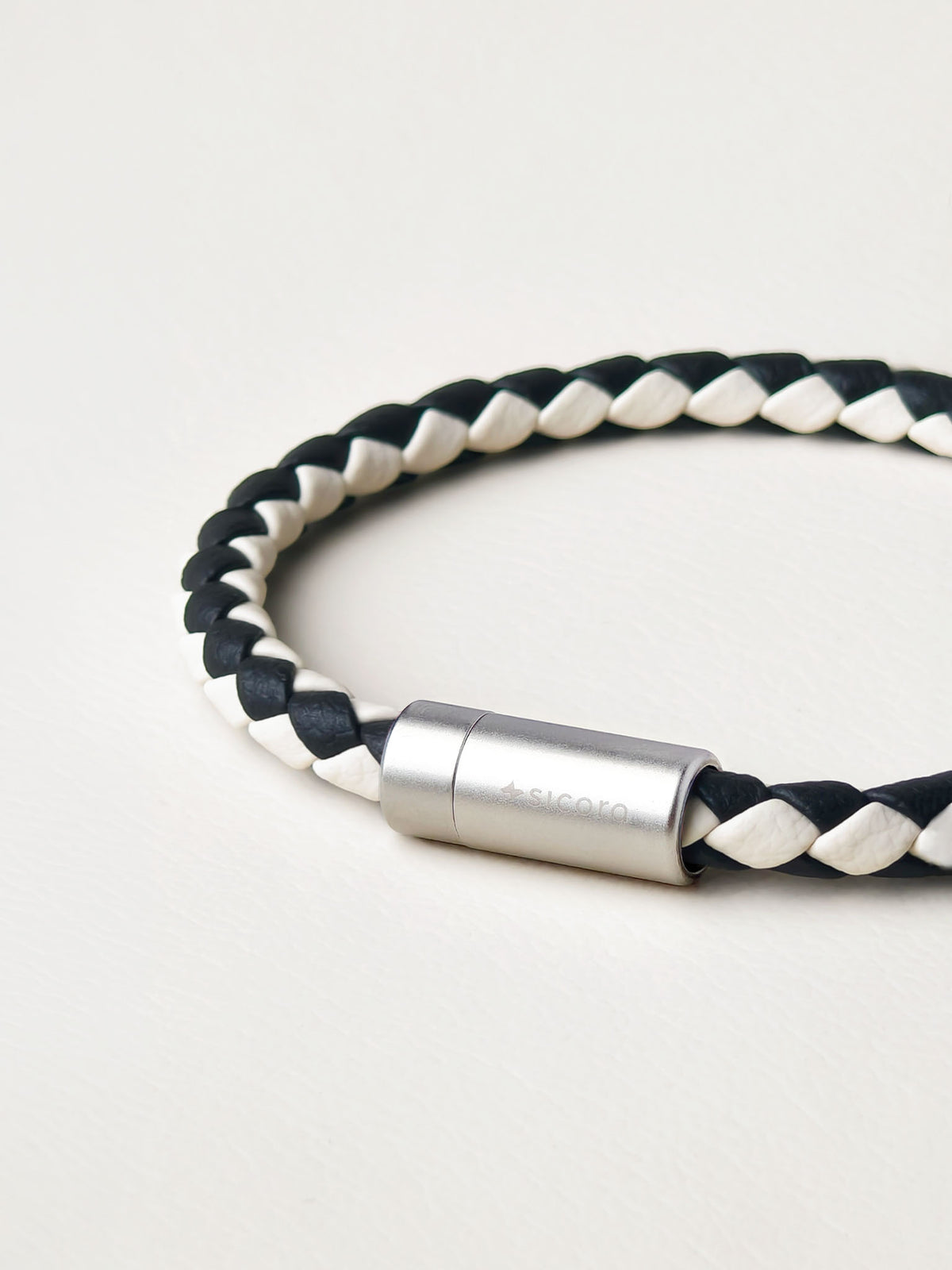 Close-up of a sicora cream and black duo-tone braided silio silicone vegan leather bracelet with a stainless steel metal magnetic clasp