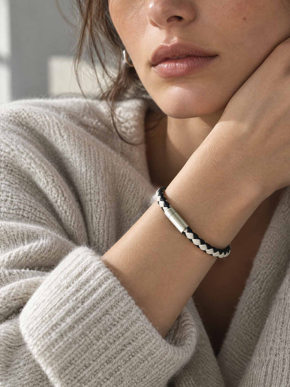 A close-up lifestyle shot of a woman wearing a sicora cream black two-tone braided silio silicone vegan leather bracelet with a stainless steel metal magnetic clasp on her wrist.