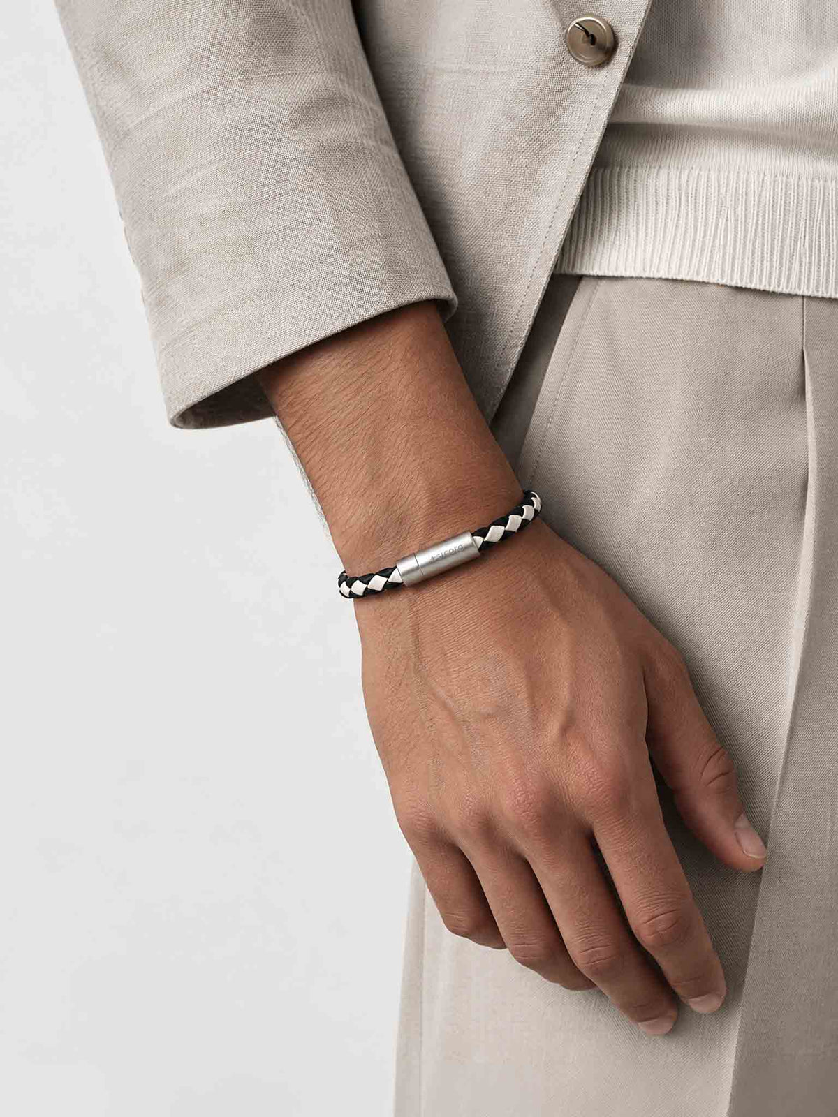 A close-up of a man's wrist wearing a sicora cream black two-tone braided leather bracelet with a stainless steel metal cylinder clasp.