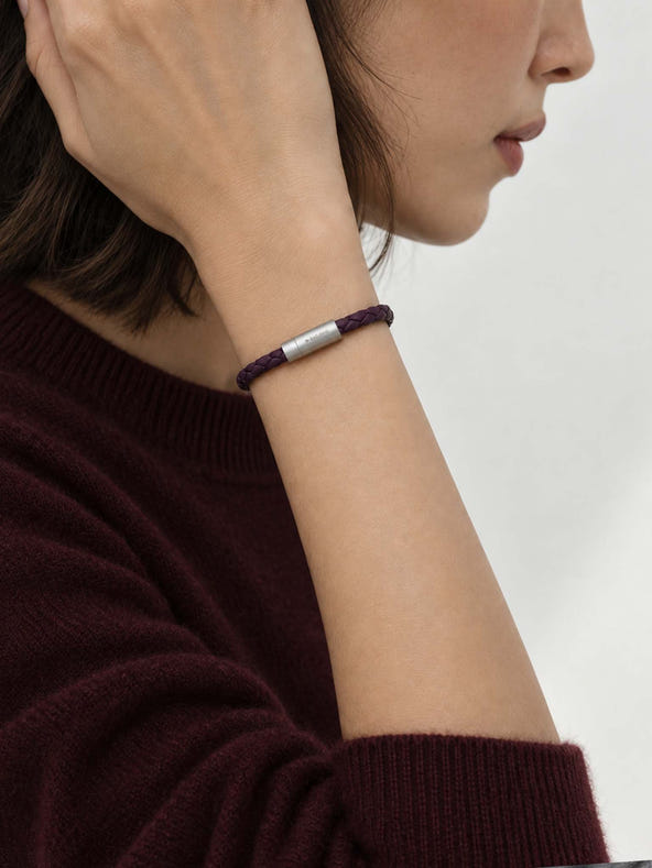 A close-up lifestyle shot of a woman wearing a sicora dark cherry purple braided silio silicone vegan leather bracelet with a stainless steel metal magnetic clasp on her wrist.