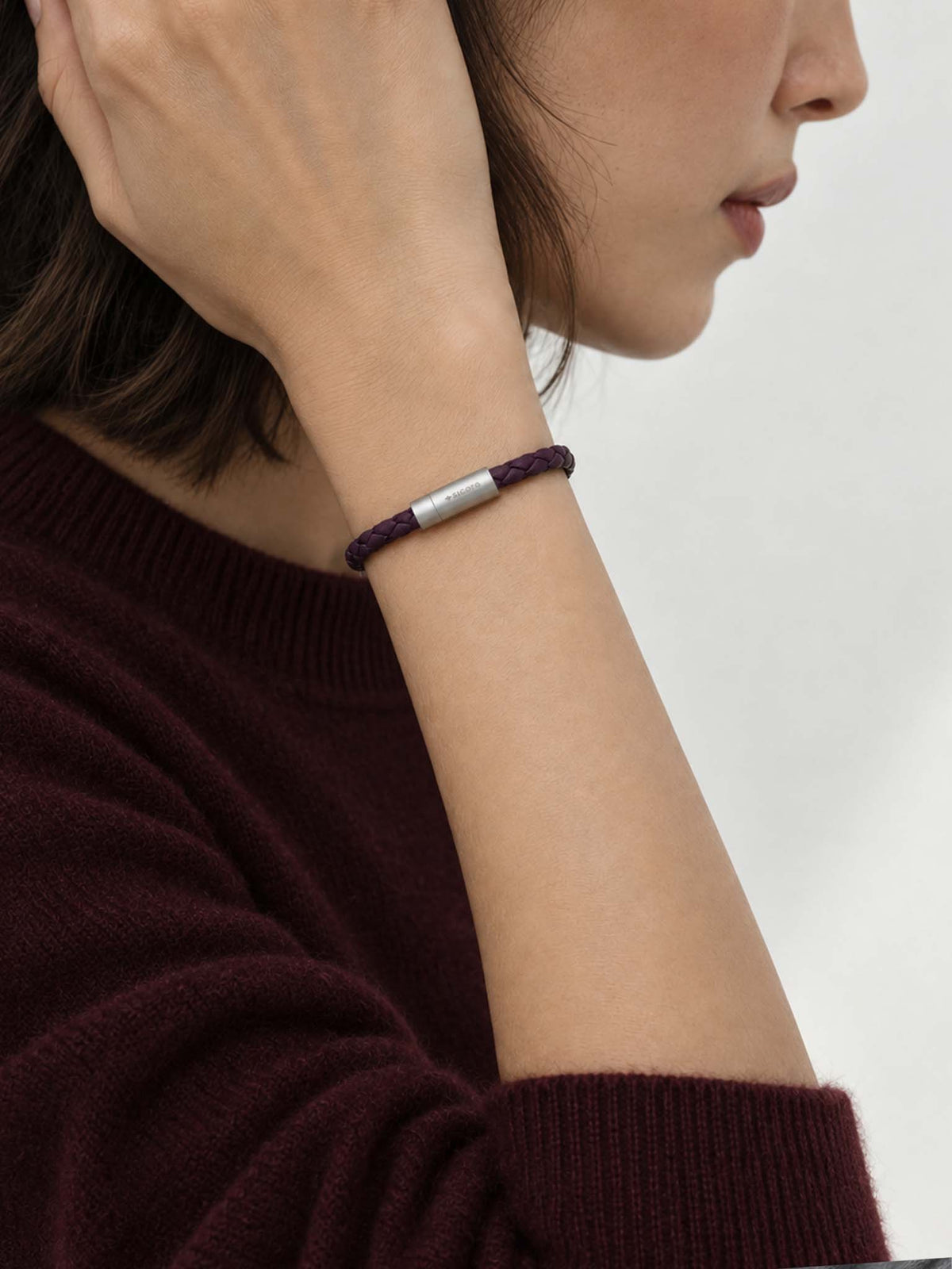 A close-up lifestyle shot of a woman wearing a sicora dark cherry purple braided silio silicone vegan leather bracelet with a stainless steel metal magnetic clasp on her wrist.