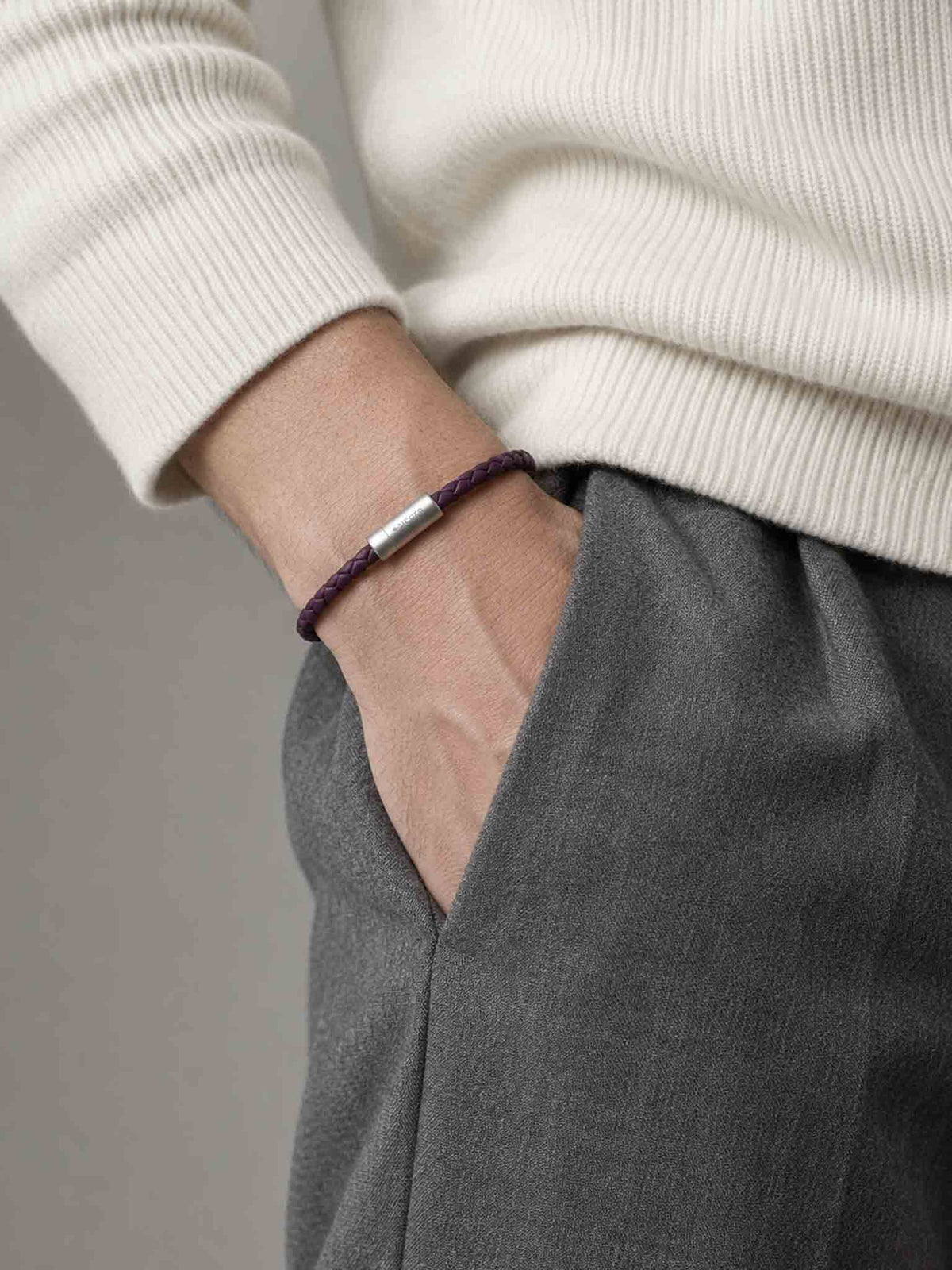 A close-up of a man's wrist wearing a sicora dark cherry purple braided leather bracelet with a stainless steel metal cylinder clasp.