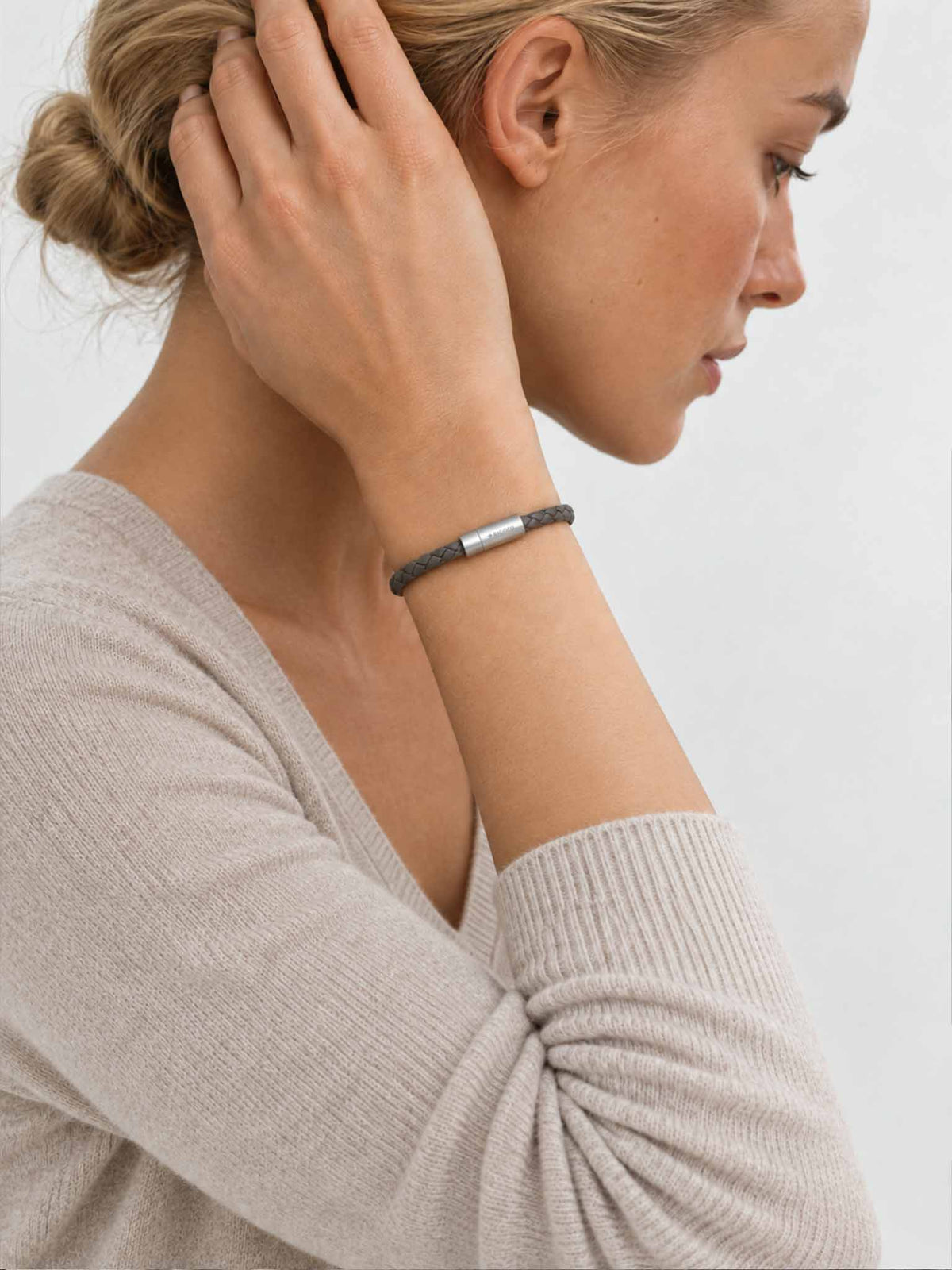A close-up lifestyle shot of a woman wearing a sicora gray / grey braided silio silicone vegan leather bracelet with a stainless steel metal magnetic clasp on her wrist.