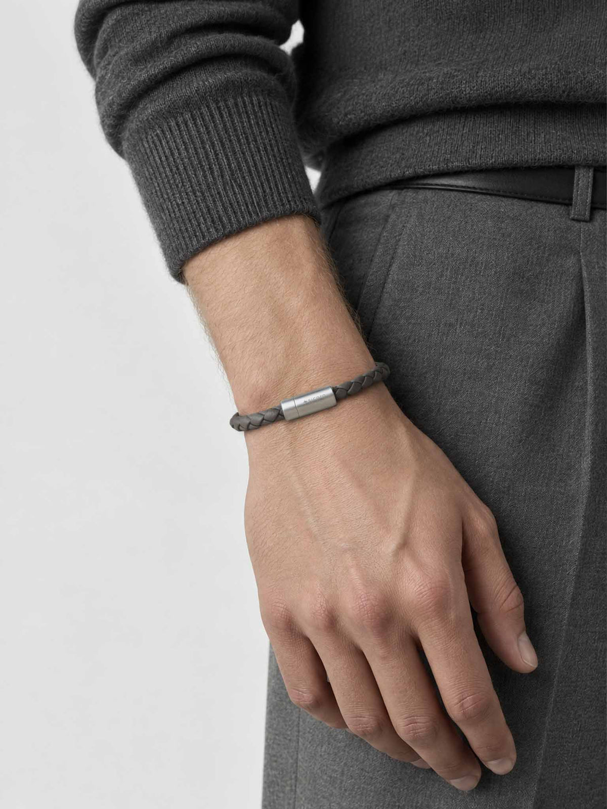 A close-up of a man's wrist wearing a sicora gray / grey braided leather bracelet with a stainless steel metal cylinder clasp.