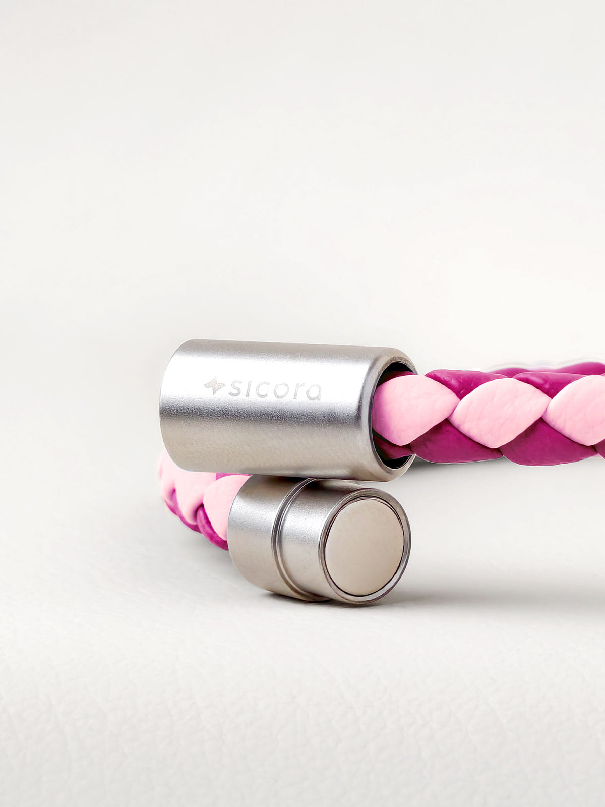 Close-up of a sicorapink and magenta two-tone braided leather bracelet with stainless steel magnetic end caps, one of which is engraved with the brand name 'sicora'.