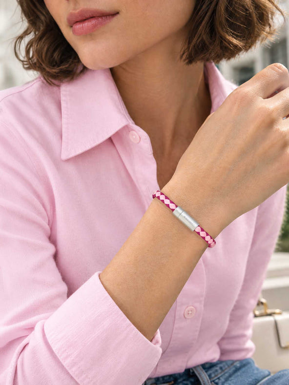 A close-up lifestyle shot of a woman wearing a sicora pink and magenta braided silio silicone vegan leather bracelet with a stainless steel metal magnetic clasp on her wrist.