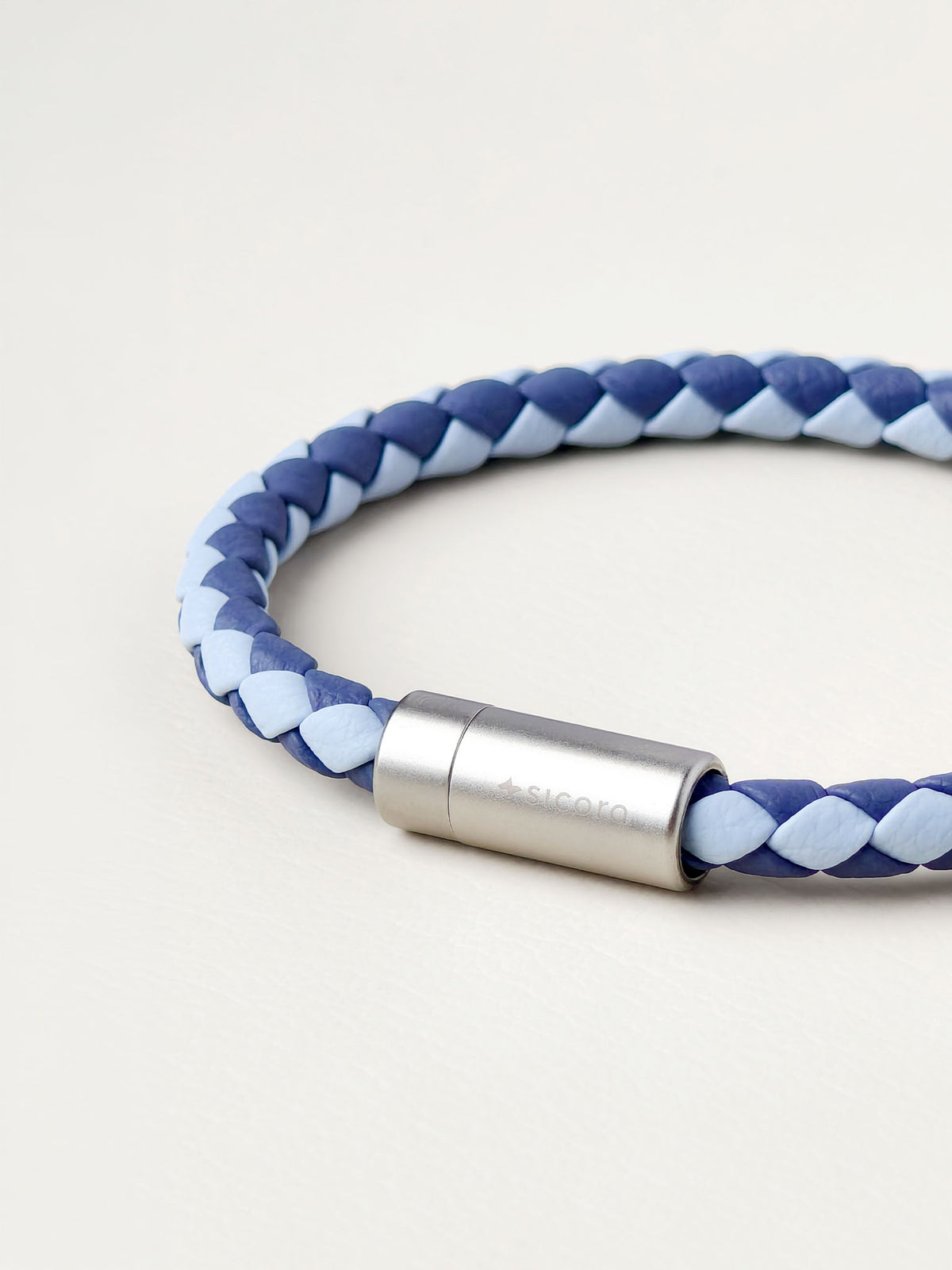 Close-up of a sicora sky blue and shadow blue duo-tone braided silio silicone vegan leather bracelet with a stainless steel metal magnetic clasp