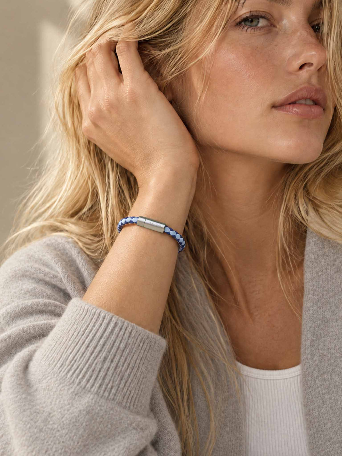 A close-up lifestyle shot of a woman wearing a sicora sky blue and shadow blue braided silio silicone vegan leather bracelet with a stainless steel metal magnetic clasp on her wrist.