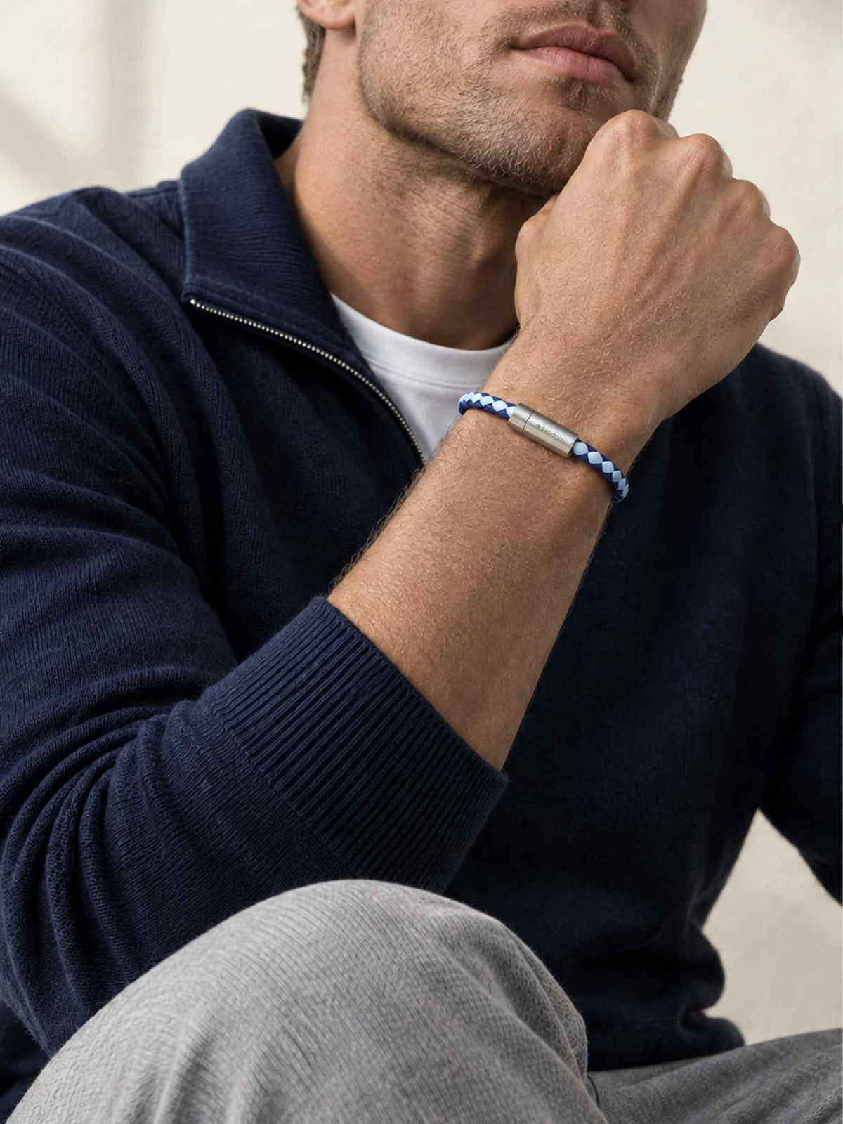 A close-up of a man's wrist wearing a sicora sky blue and shadow blue two-tone braided leather bracelet with a stainless steel metal cylinder clasp.