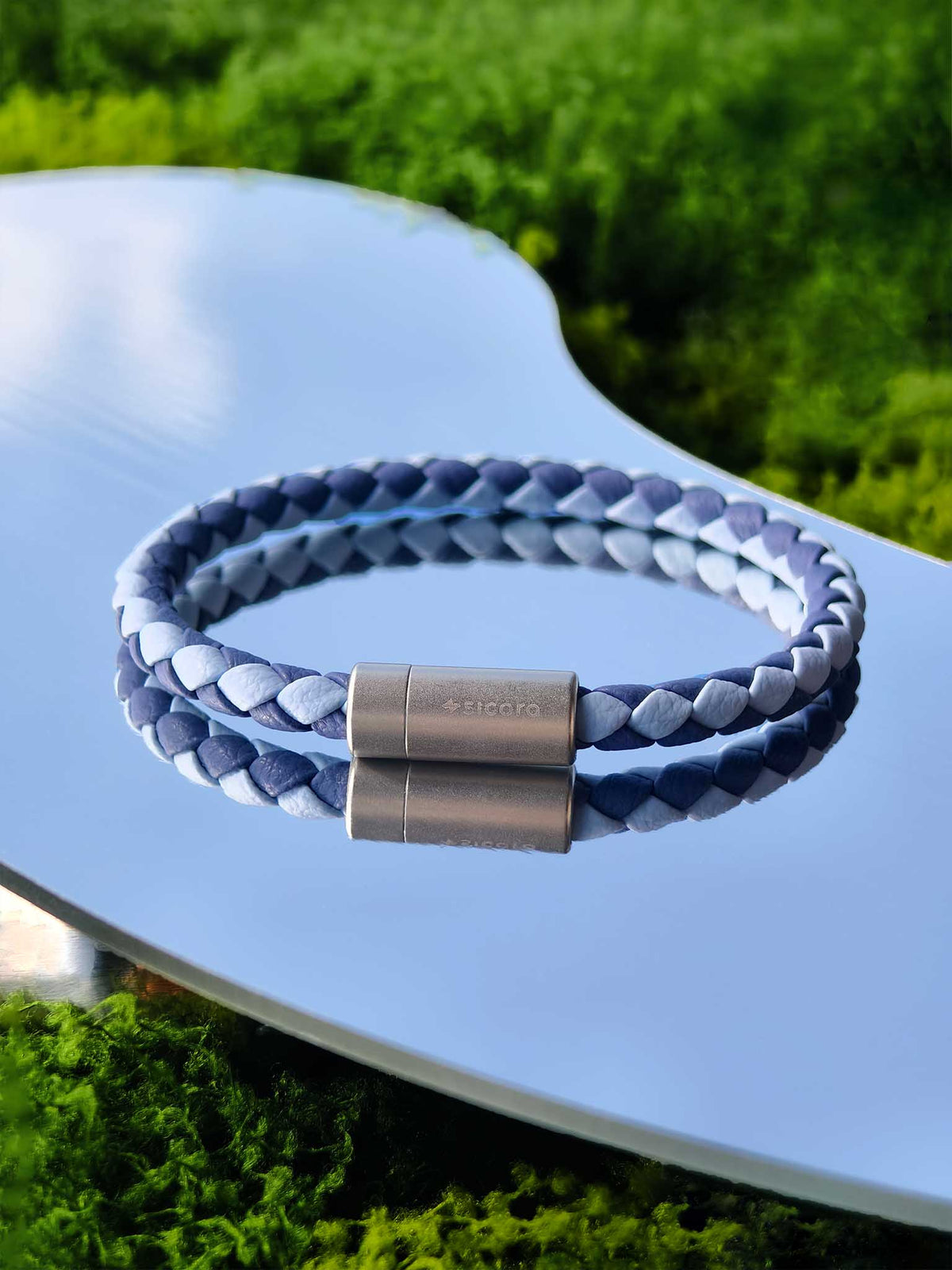 sicora sky blue and shadow blue duo-tone braided silio silicone vegan leather bracelet with a stainless steel metal magnetic clasp, on a reflective surface