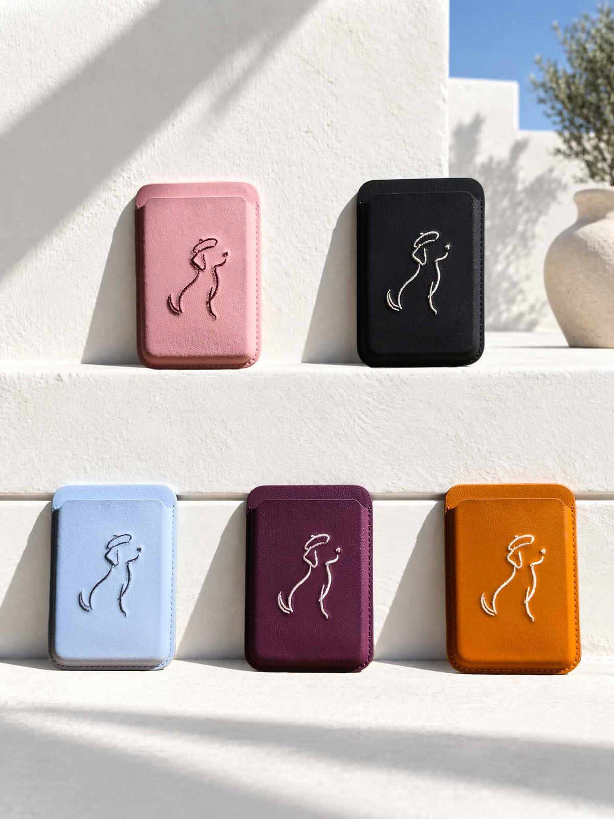 Five sicora graphic magnetic card wallets (The Artist Collection) in pink, black, light blue, burgundy, and orange, each wallet has a minimalist line-art embroidery on the front.