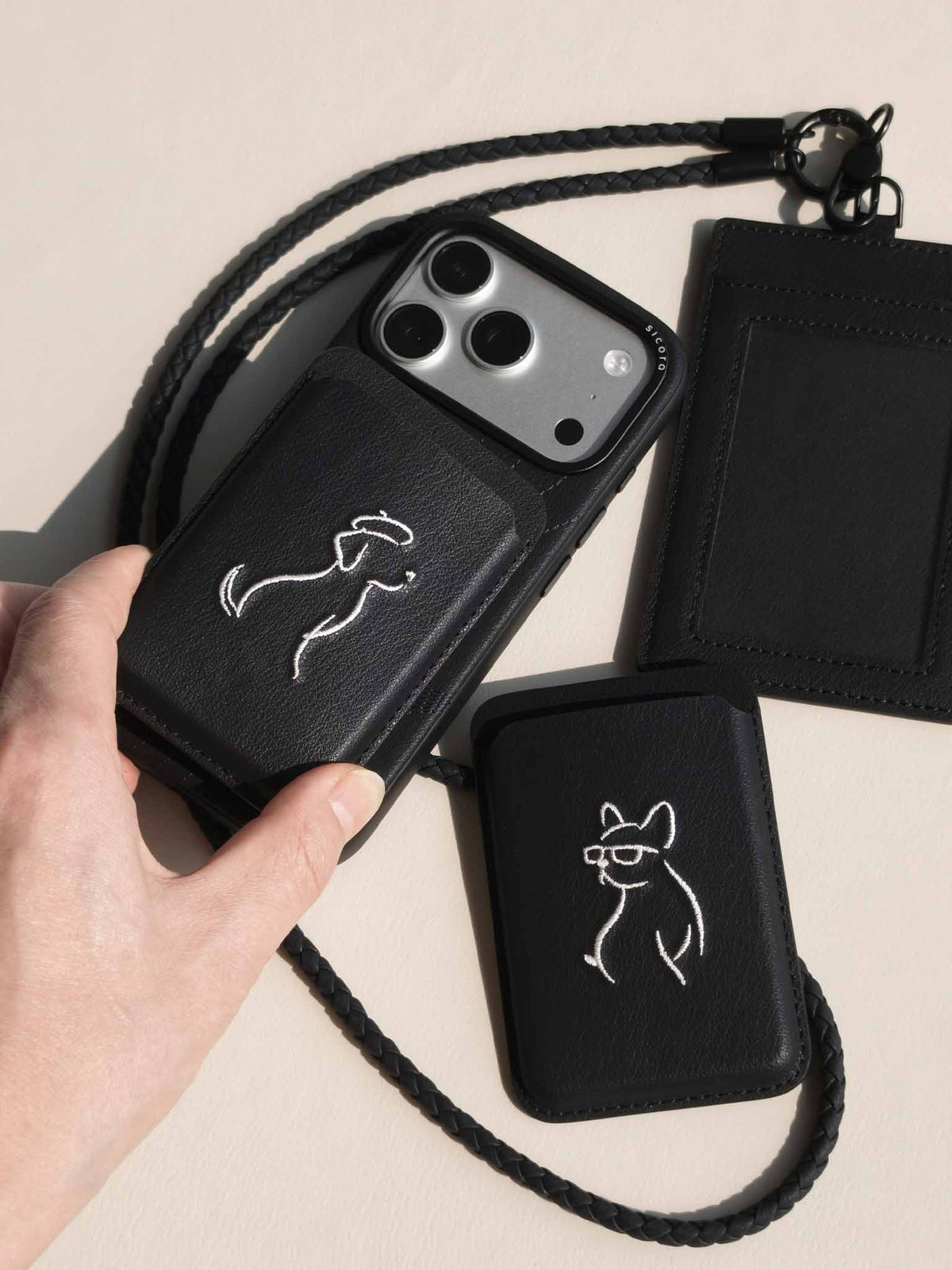 Hand holding sicora vegan leather graphic magnetic card wallet in black with cream white embroidered dog line-drawing