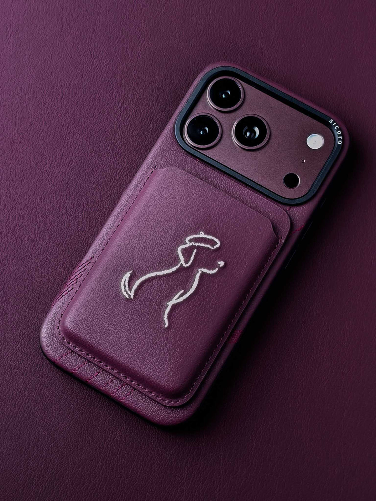 sicora vegan leather graphic magnetic card wallet in cherry purple with cream white embroidered dog line-drawing, on an iPhone 18 pro case