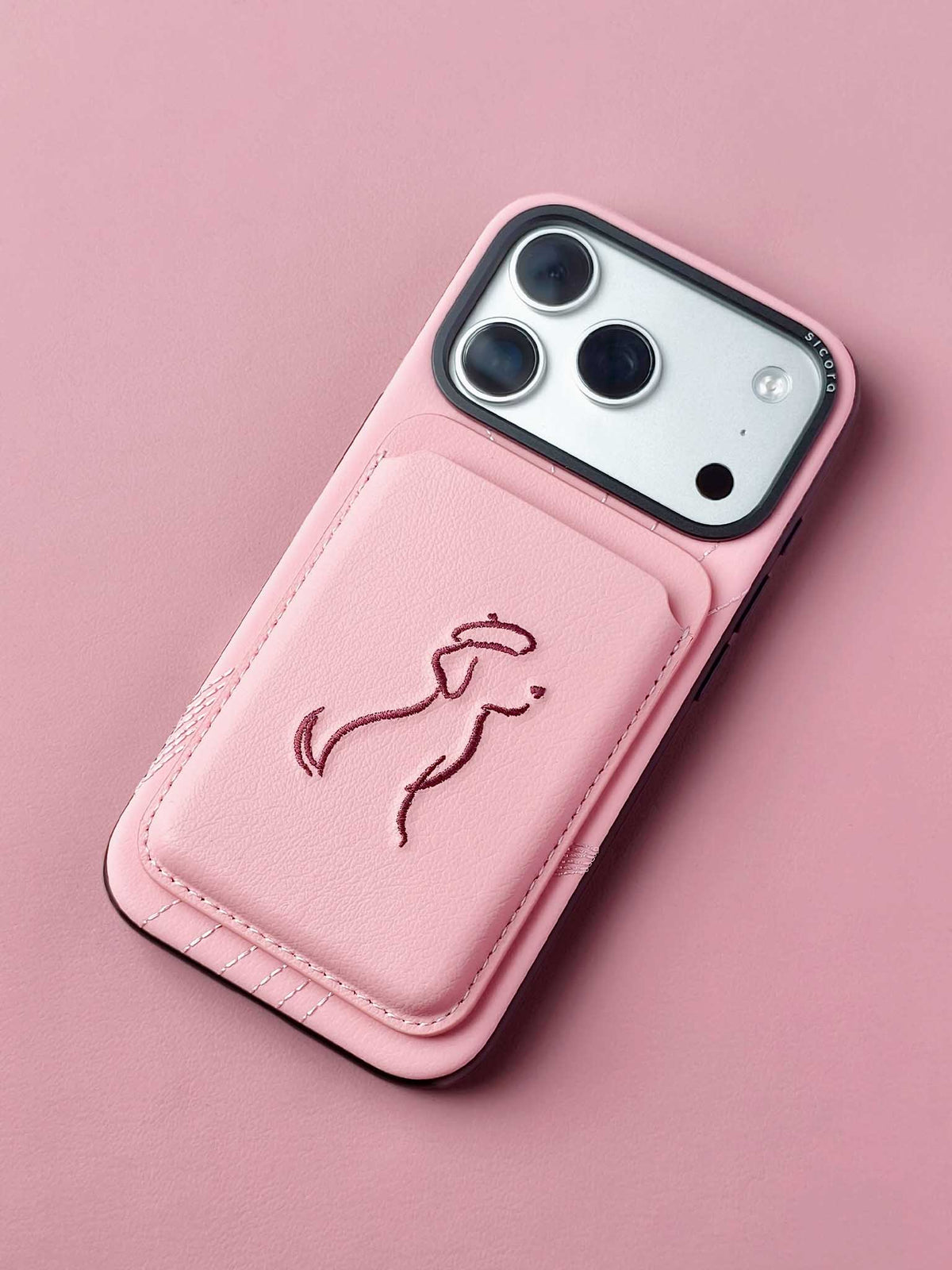sicora vegan leather graphic magnetic card wallet in pink with dark burgundy embroidered dog line-drawing, on an iPhone 18 / 17 pro case.