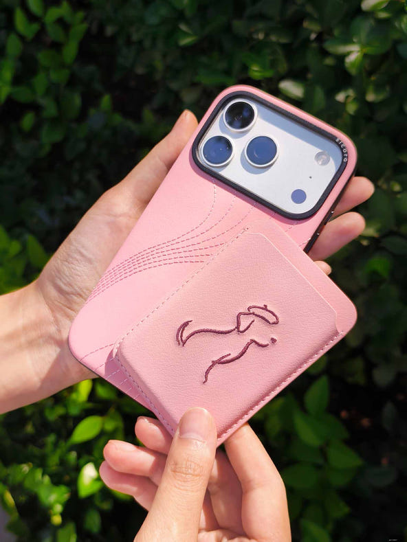 Hands holding a sicora vegan leather graphic magnetic card wallet in pink with dark burgundy embroidered dog line-drawing & a sicora iPhone 18 / 17 pro case