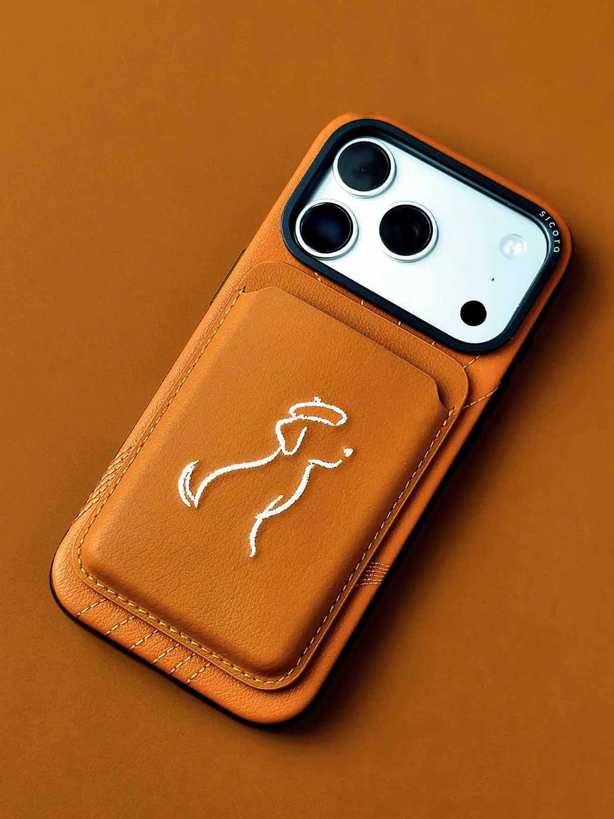 sicora vegan leather graphic magnetic card wallet in toffee gold brown with cream white embroidered dog line-drawing on a sicora iPhone 18 / 17 pro case
