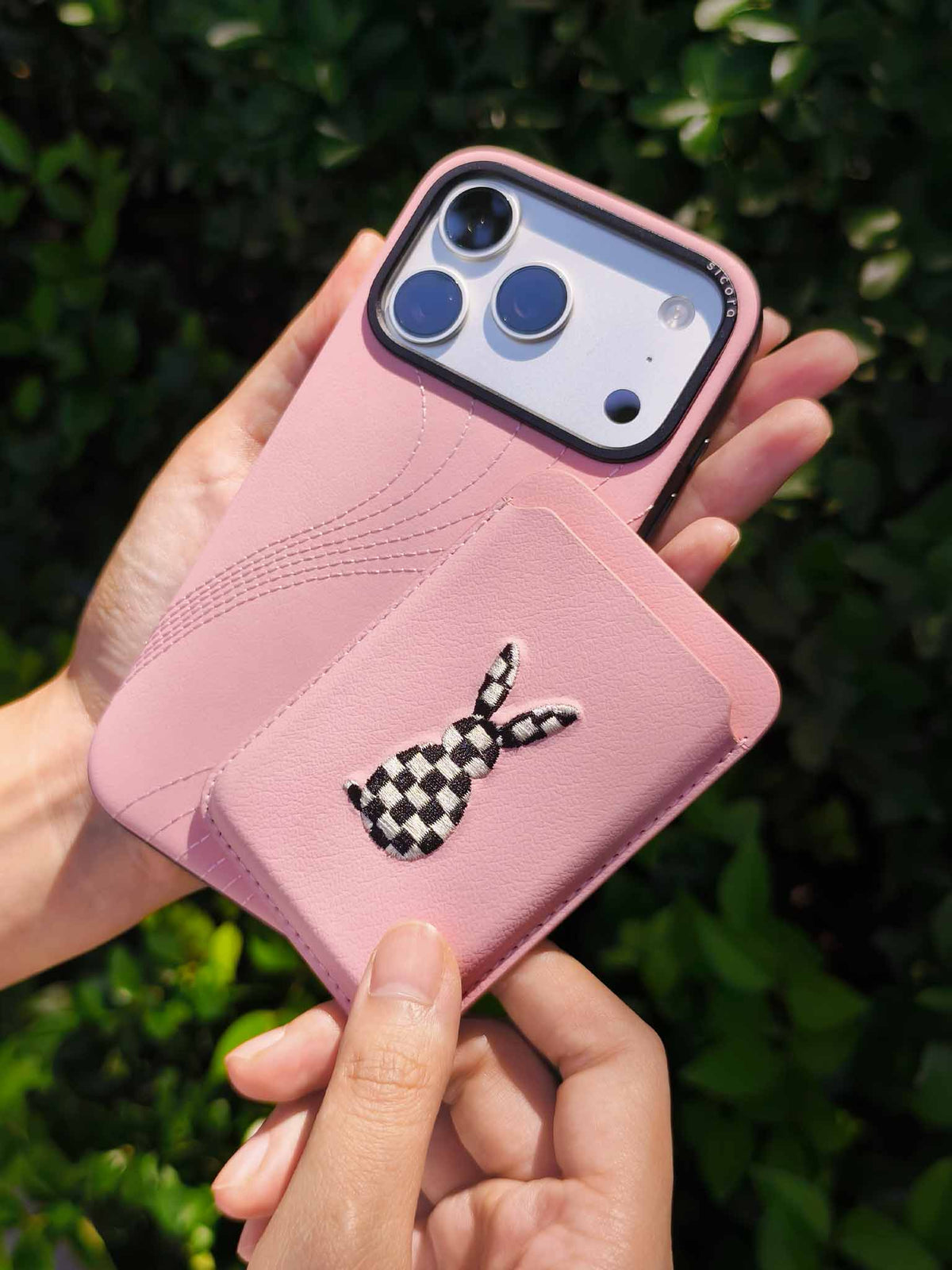 Hands holding a sicora vegan leather graphic magnetic card wallet in pink with black and white embroidered rabbit artwork & a sicora iPhone 18 pro case