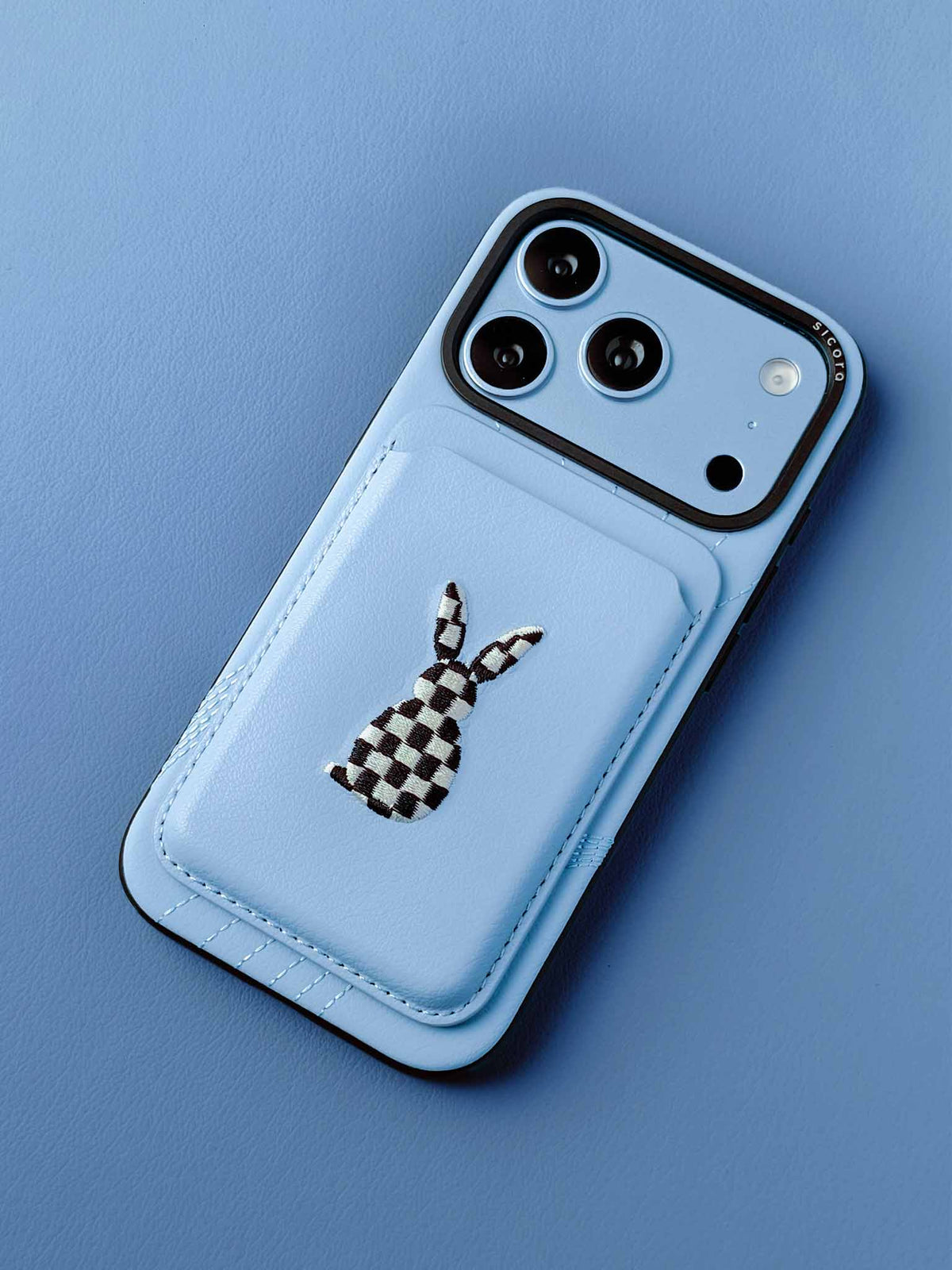 sicora vegan leather graphic magnetic card wallet in light blue with black and white embroidered rabbit artwork on a sicora iPhone 18 pro case