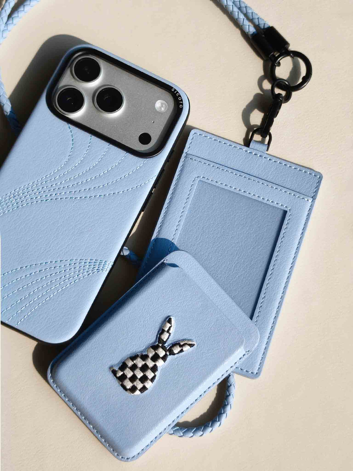 Flat-lay of sicora vegan leather accessories: iPhone 18 pro case, magnetic card wallet, and ID badge holder with lanyard