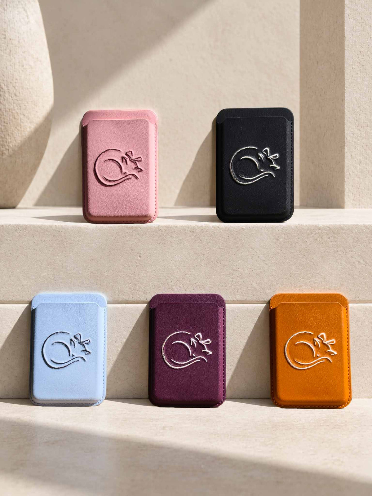 Five sicora graphic magnetic card wallets (The Muse Collection) in pink, black, light blue, burgundy, and orange, each wallet has a minimalist line-art embroidery on the front.