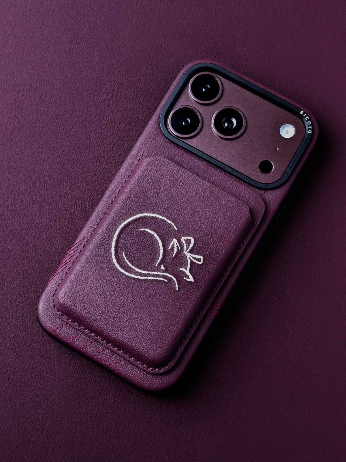 sicora vegan leather graphic magnetic card wallet in cherry purple with cream white embroidered cat line-drawing on a sicora iPhone 18 pro case