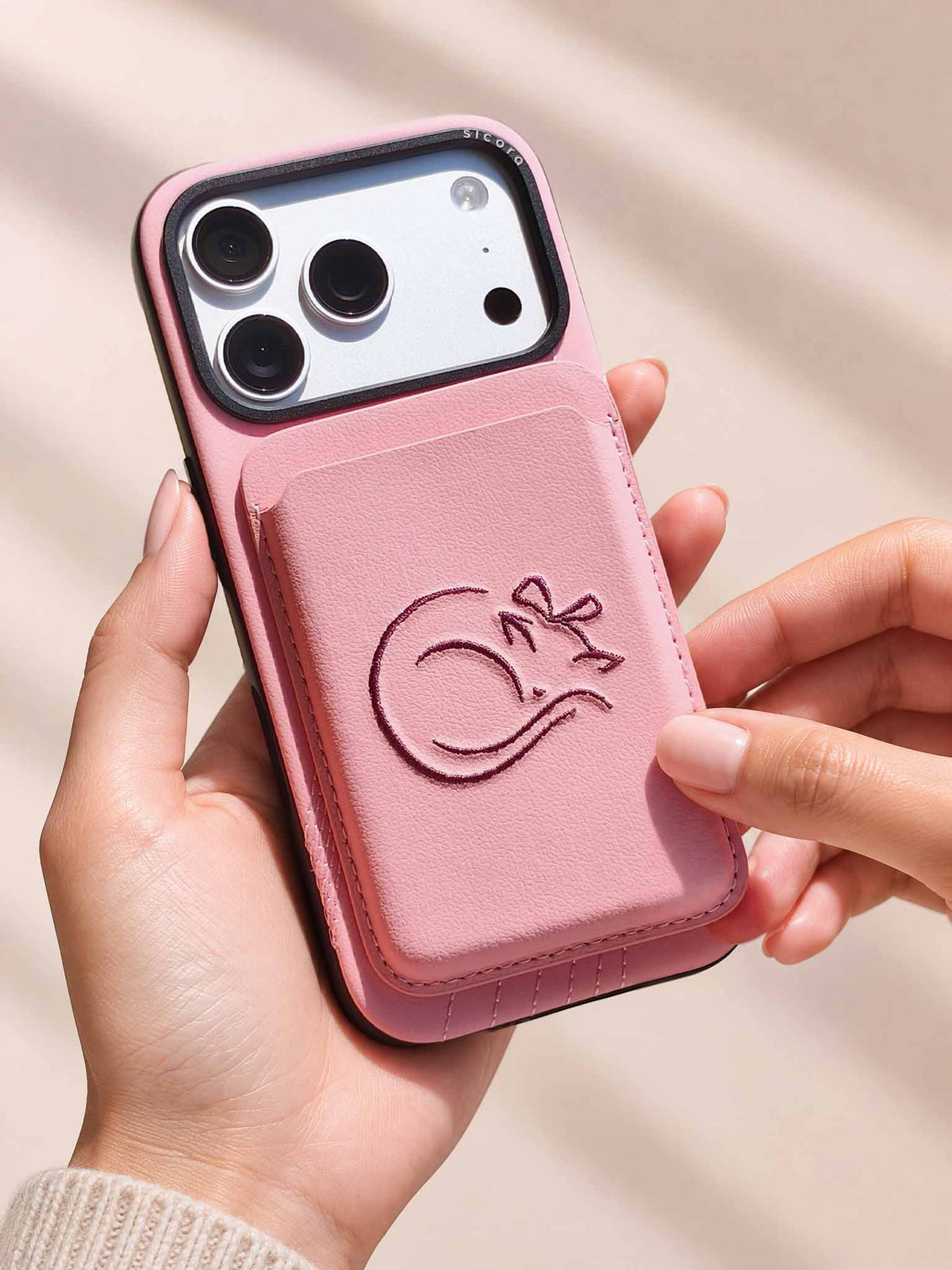 Hands holding a sicora vegan leather graphic magnetic card wallet in pink with dark burgundy embroidered cat line-drawing & a sicora iPhone 18 pro case