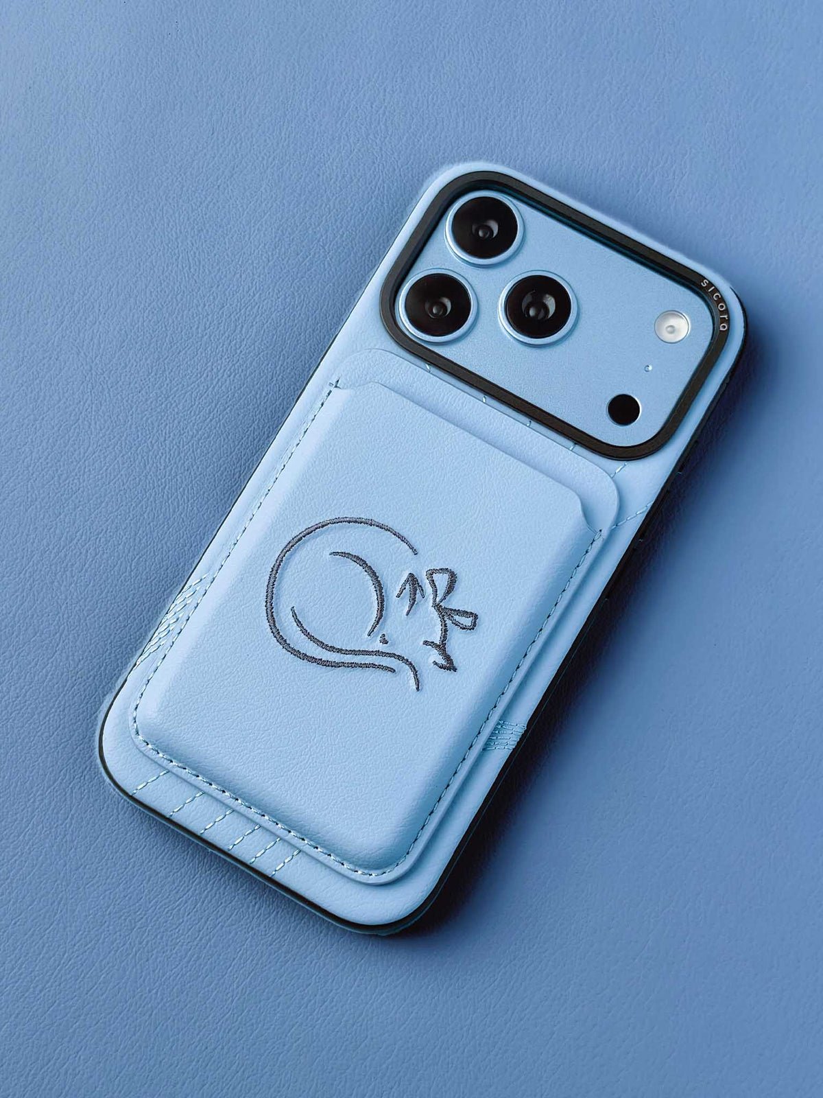 sicora vegan leather graphic magnetic card wallet in sky blue with grey blue embroidered cat line-drawing on a sicora iPhone 18 pro case