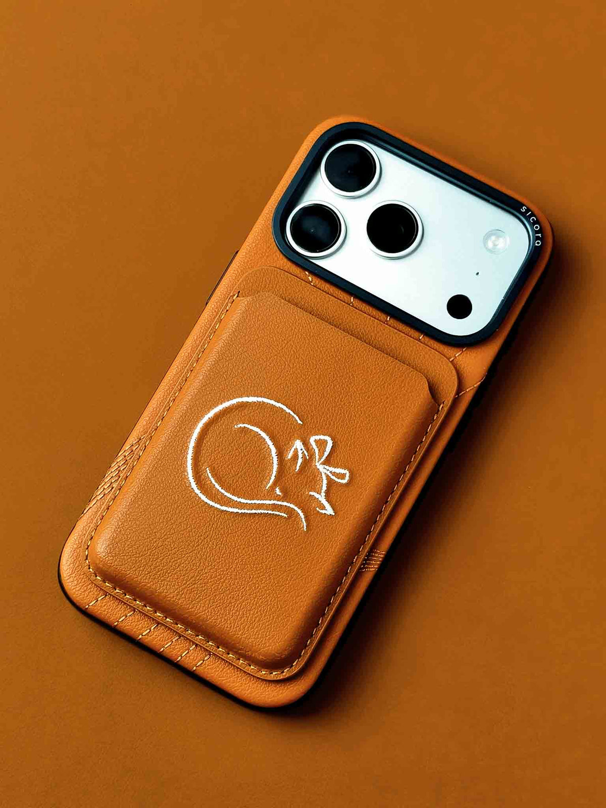 sicora vegan leather graphic magnetic card wallet in toffee gold brown with cream white embroidered cat line-drawing on a iPhone 18 / 17 pro case