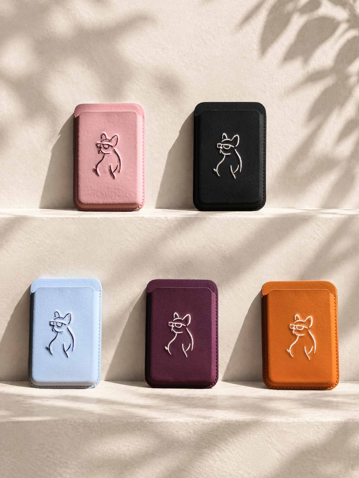 Five sicora graphic magnetic card wallets (The Rebel Collection) in pink, black, light blue, burgundy, and orange, each wallet has a minimalist line-art embroidery on the front.