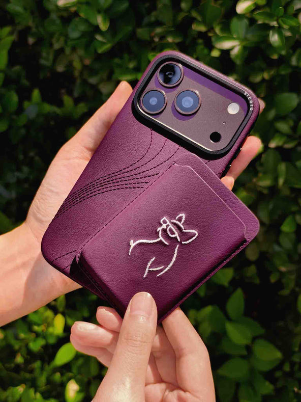 Hands holding a sicora vegan leather graphic magnetic card wallet in cherry purple with cream white embroidered dog line-drawing & a sicora iPhone 18 pro case