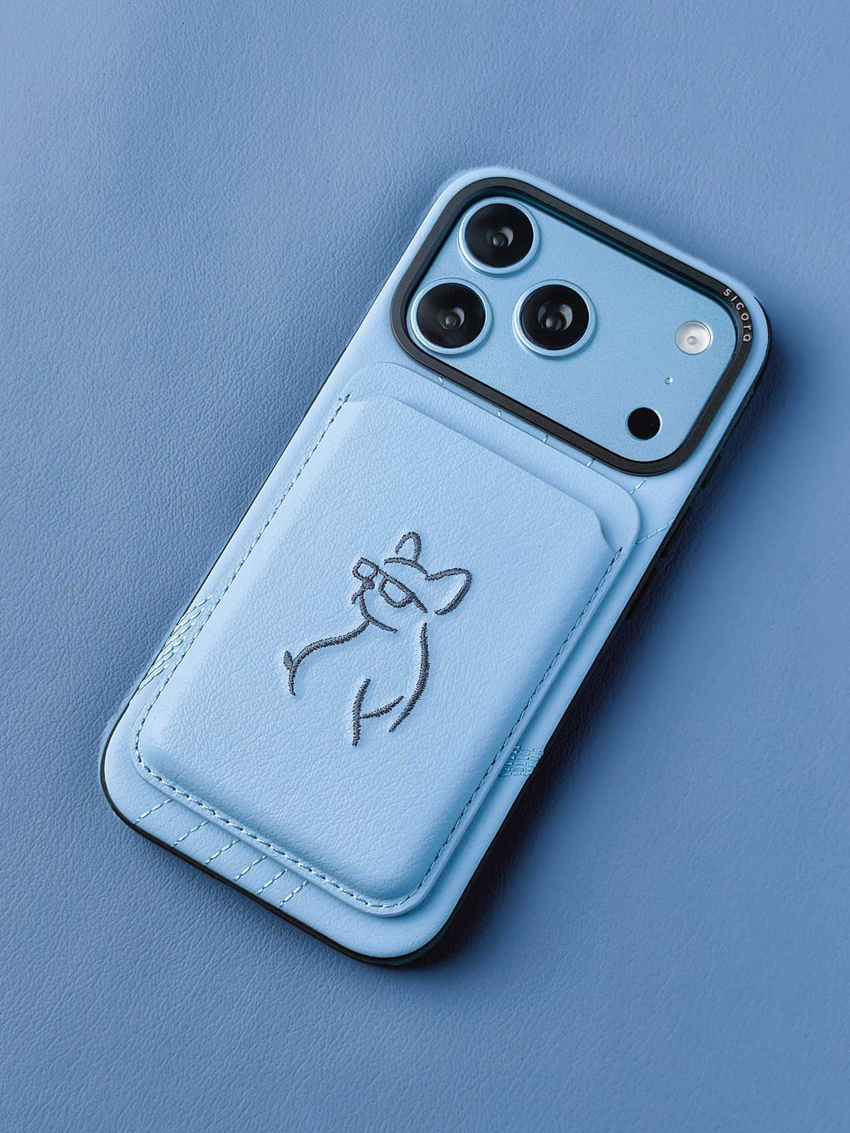 sicora vegan leather graphic magnetic card wallet in sky blue with grey blue embroidered dog line-drawing on a sicora iPhone 18 pro case