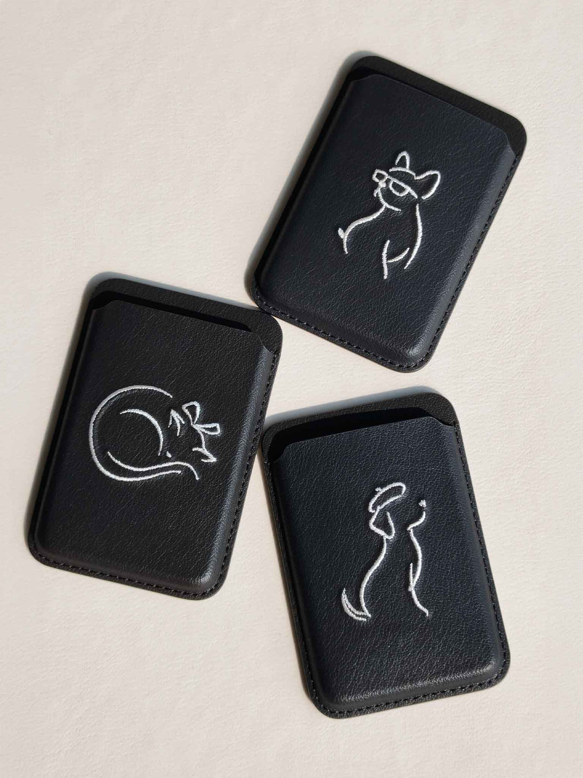 Three sicora vegan leather graphic magnetic card wallets in black with cream white embroidered minimalist animal artworks