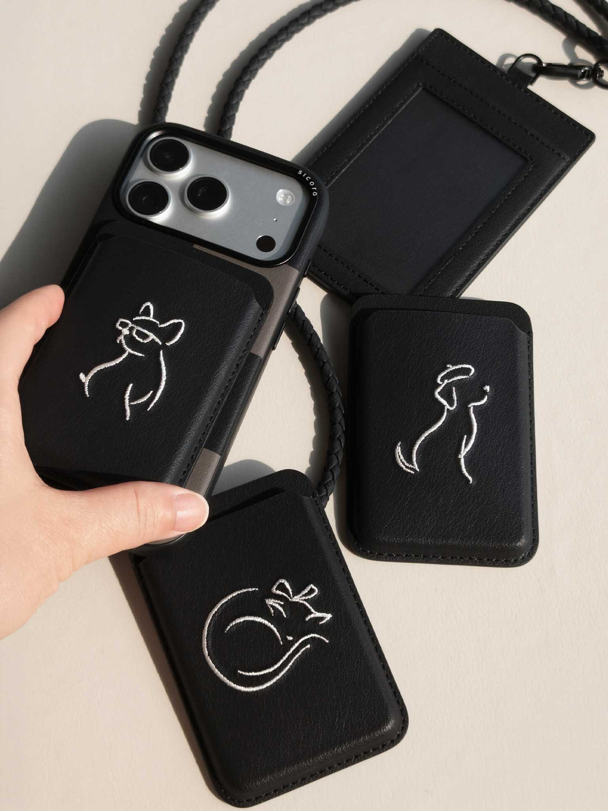 Product shot of black sicora vegan leather accessories: iPhone 18 / 17 pro case, magnetic card wallets, and ID badge holder with lanyard