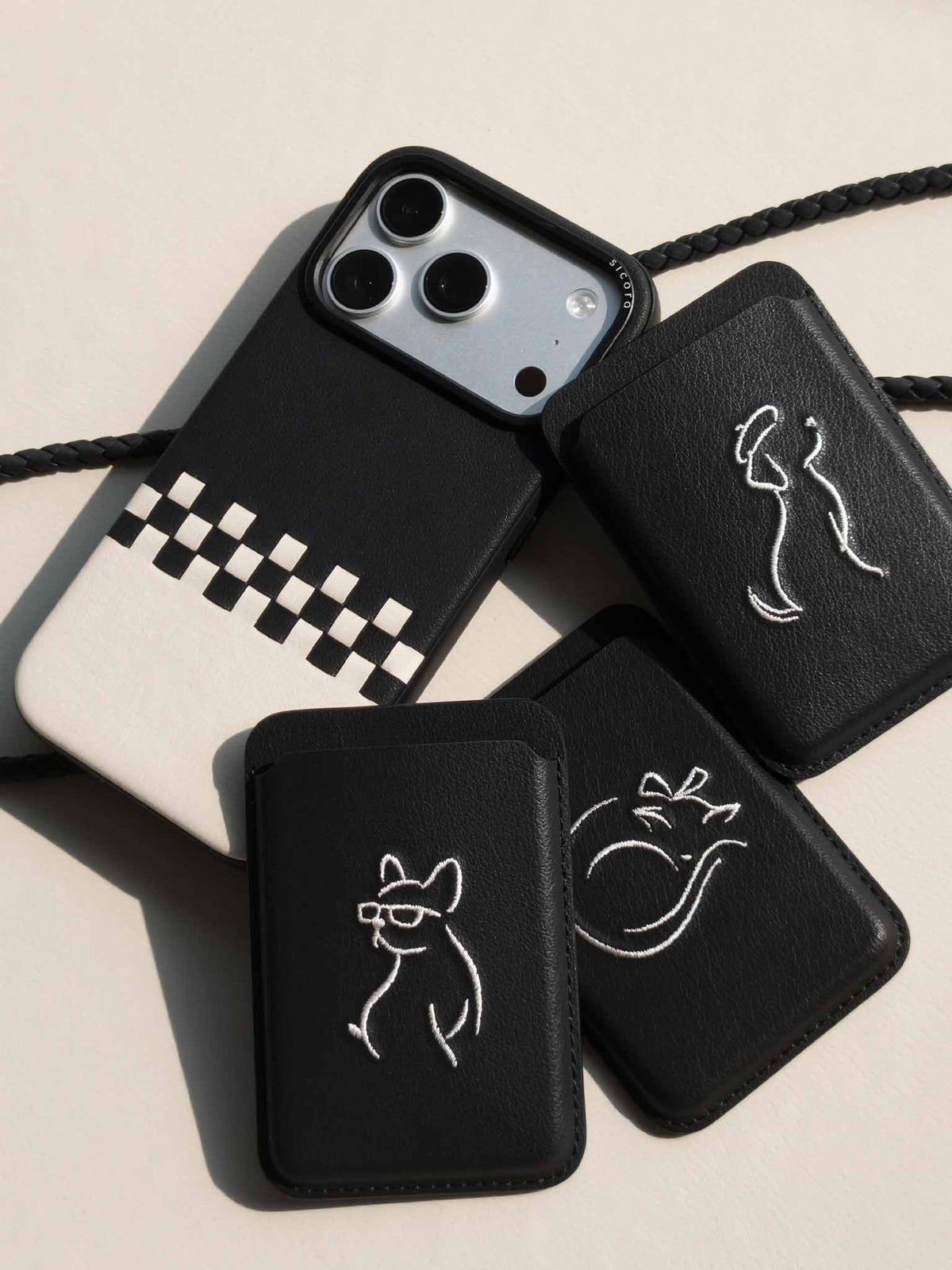 Flat-lays of black sicora vegan leather accessories: iPhone 18 / 17 pro case, magnetic card wallets, and lanyard