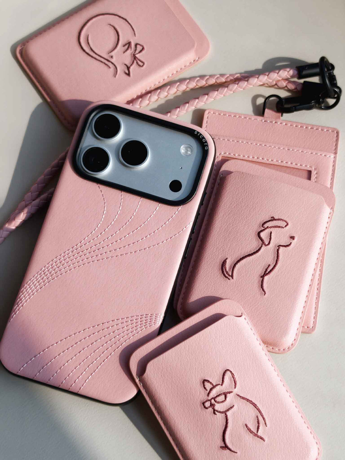 Flat-lays of pink sicora vegan leather accessories: iPhone 18 / 17 pro case, magnetic card wallets, and ID badge holder with lanyard