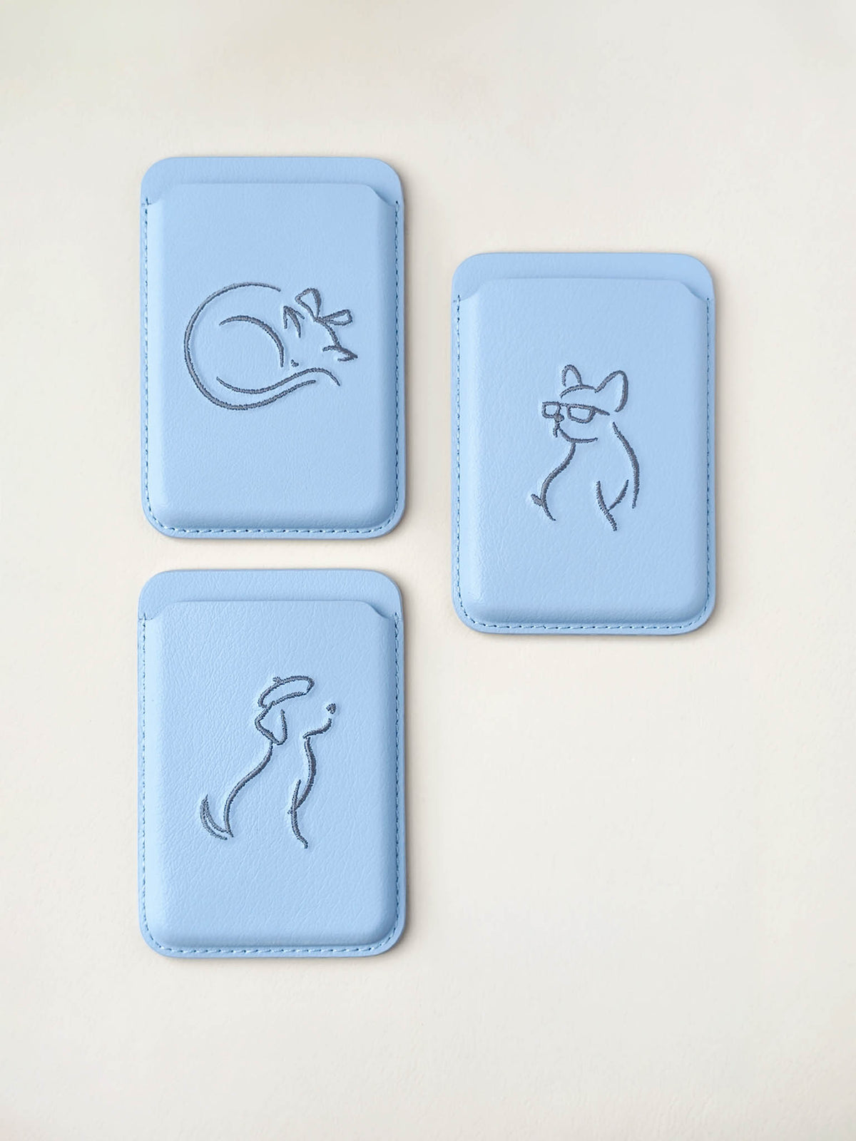 Three sicora vegan leather graphic magnetic card wallets in sky blue with grey blue embroidered minimalist animal artworks