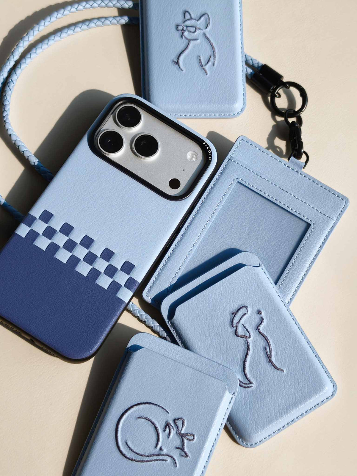 Flat-lays of sky blue sicora vegan leather accessories: iPhone 18 / 17 pro case, magnetic card wallets, and ID badge holder with lanyard