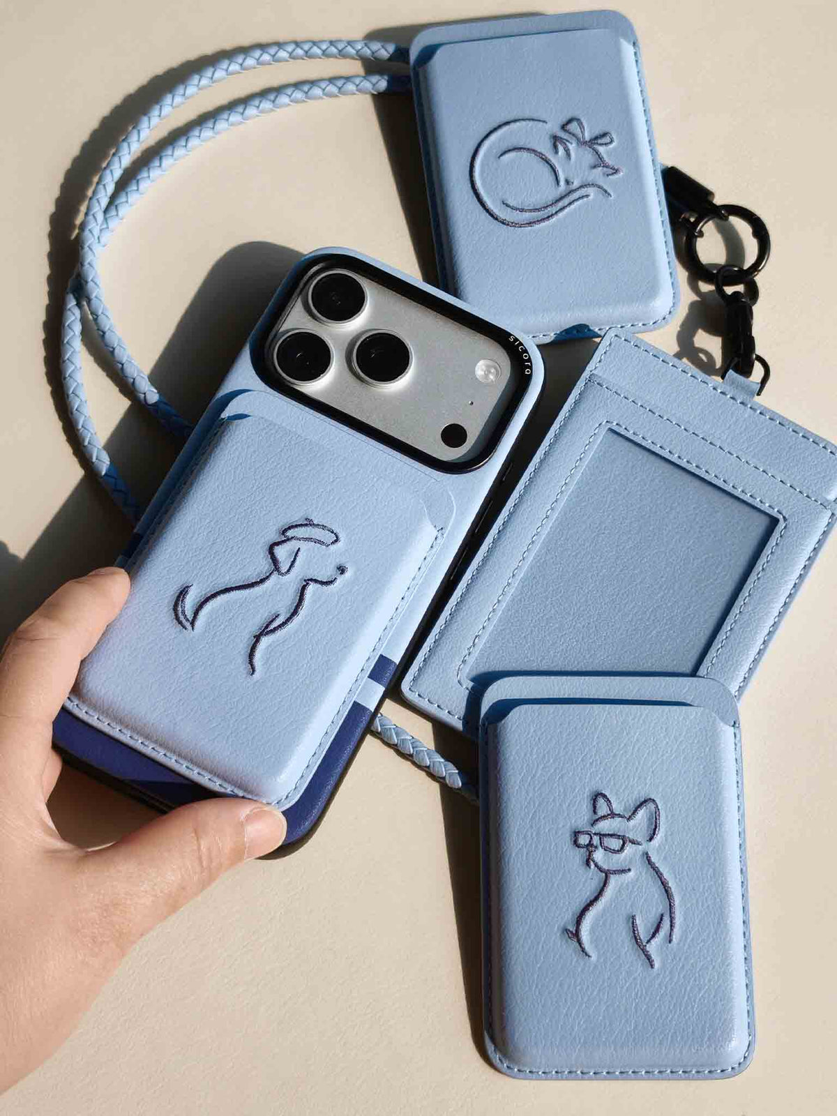 Product shot of sky blue sicora vegan leather accessories: iPhone 18 / 17 pro case, magnetic card wallets, and ID badge holder with lanyard