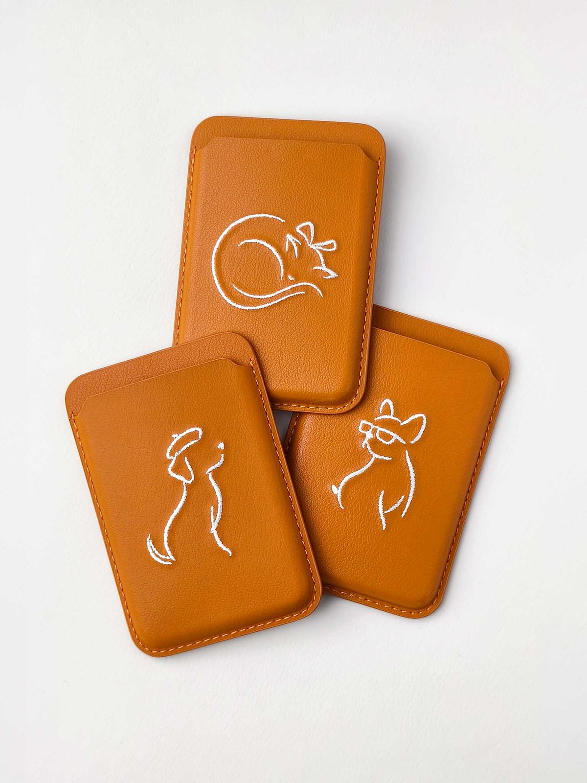 Three sicora vegan leather graphic magnetic card wallets in toffee gold brown with cream white embroidered minimalist animal artworks