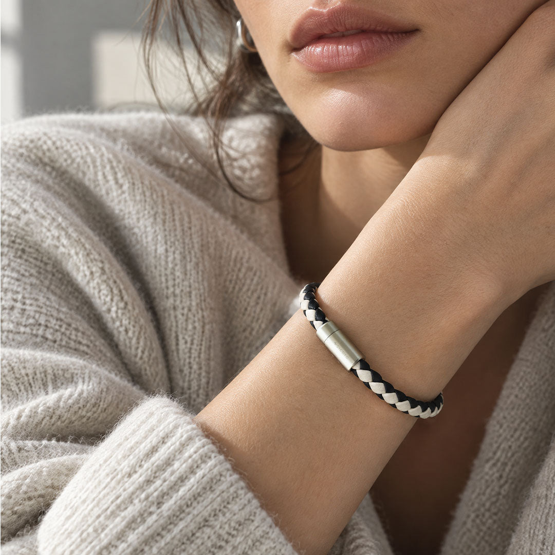 A close-up lifestyle shot of a woman wearing a sicora cream black two-tone braided silio silicone vegan leather bracelet with a stainless steel metal magnetic clasp on her wrist.