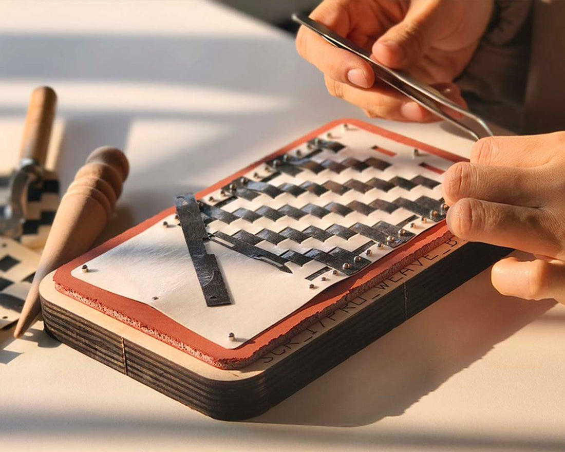 Person working on woven leather patterns with tools on a table