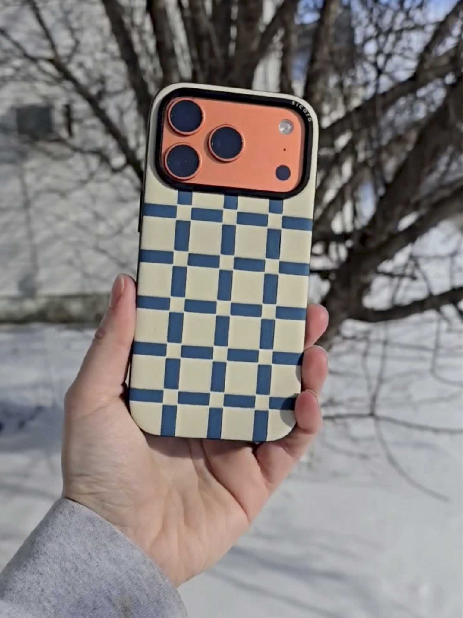 Hand holding a sicora gridplay iPhone case against a snowy background