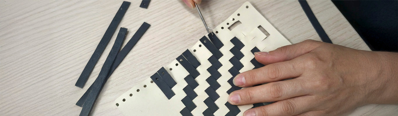 A craftsman assembling a black and white zigzag patterned leather surface with tools on a wooden surface.